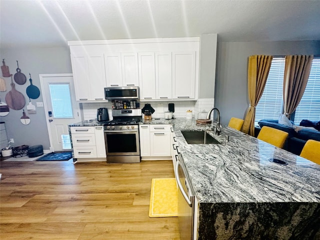 kitchen featuring sink, stainless steel appliances, light hardwood / wood-style floors, white cabinets, and decorative backsplash