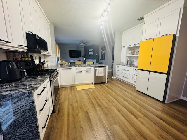 kitchen featuring light hardwood / wood-style flooring, dark stone countertops, appliances with stainless steel finishes, ceiling fan, and white cabinets