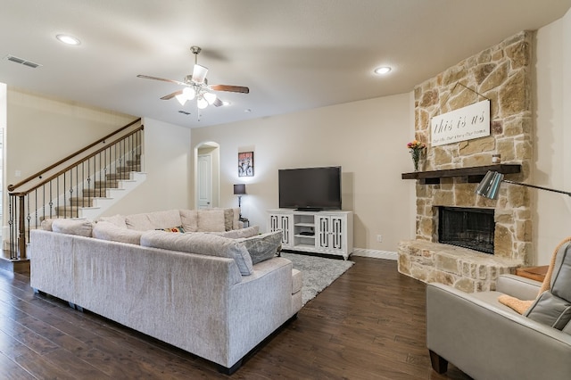 living room with a stone fireplace, dark wood-type flooring, and ceiling fan