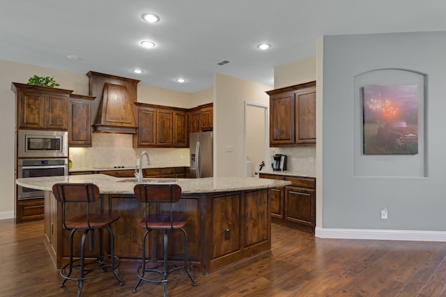 kitchen with stainless steel appliances, sink, custom range hood, and a center island with sink