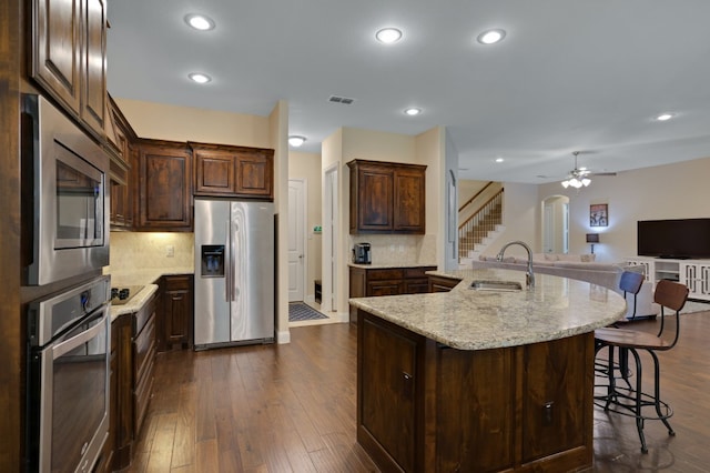 kitchen featuring sink, dark wood-type flooring, stainless steel appliances, and a center island with sink