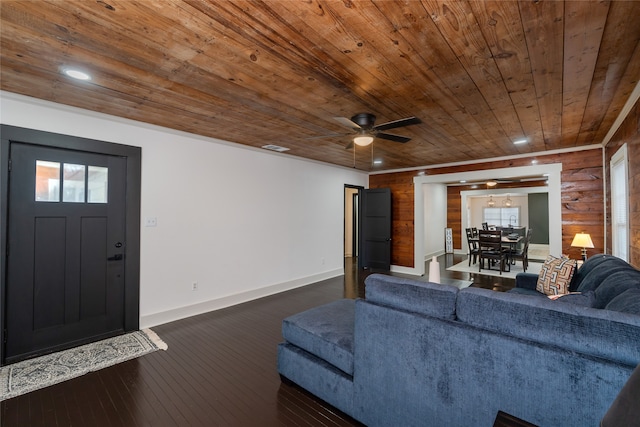 living room with dark wood-type flooring, wooden ceiling, ceiling fan, and wood walls