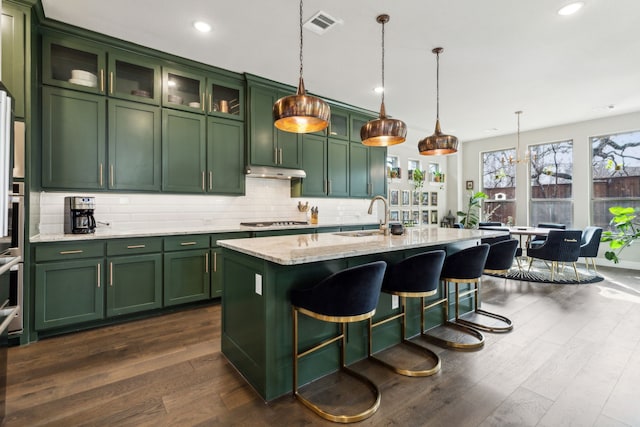 kitchen featuring under cabinet range hood, stainless steel gas stovetop, green cabinets, and a sink