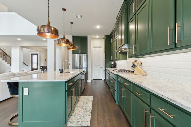 kitchen featuring sink, a kitchen island with sink, a kitchen breakfast bar, green cabinetry, and decorative light fixtures