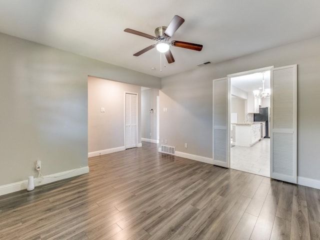 unfurnished room with ceiling fan with notable chandelier and hardwood / wood-style floors