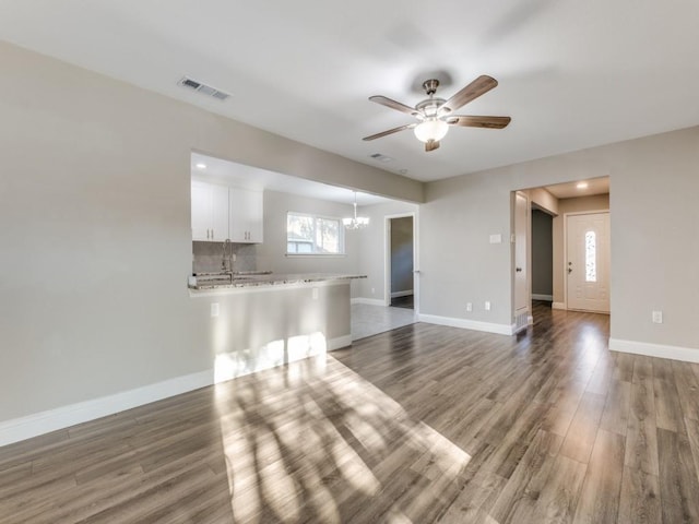 unfurnished living room featuring hardwood / wood-style floors and ceiling fan with notable chandelier