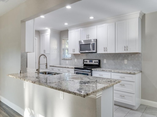 kitchen with sink, stainless steel appliances, light stone countertops, white cabinets, and kitchen peninsula