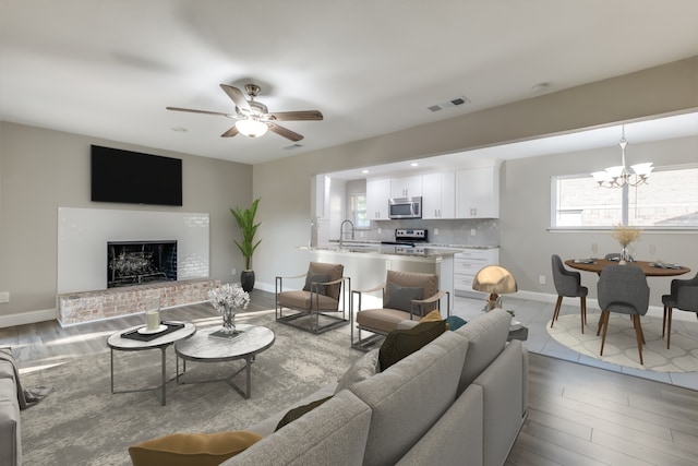 living room featuring sink, ceiling fan with notable chandelier, a fireplace, and light hardwood / wood-style flooring