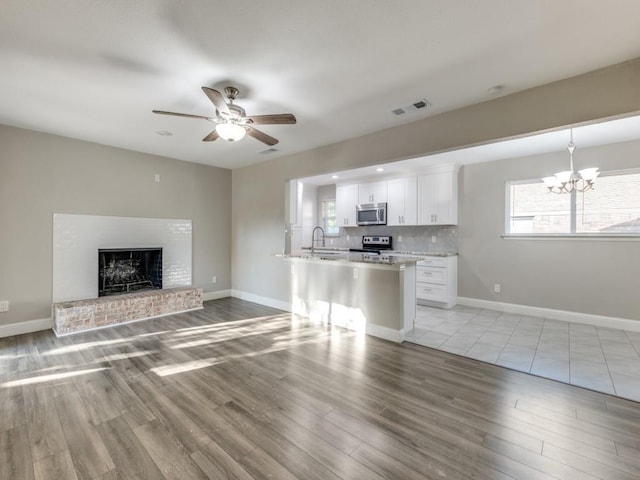 kitchen featuring pendant lighting, tasteful backsplash, white cabinets, stainless steel appliances, and a brick fireplace