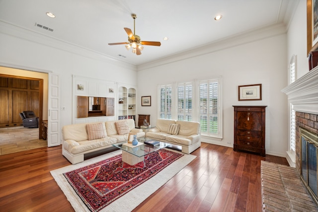 living room with dark wood-type flooring, ceiling fan, ornamental molding, and a brick fireplace