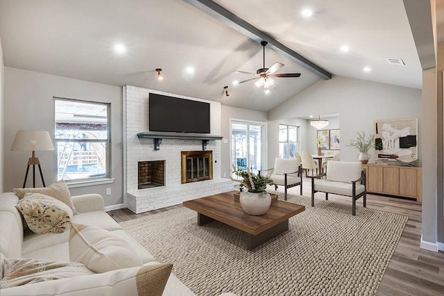 living room featuring a healthy amount of sunlight, a brick fireplace, vaulted ceiling with beams, and dark hardwood / wood-style flooring