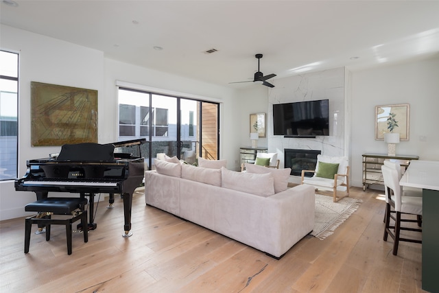 living room featuring ceiling fan, a fireplace, and light wood-type flooring