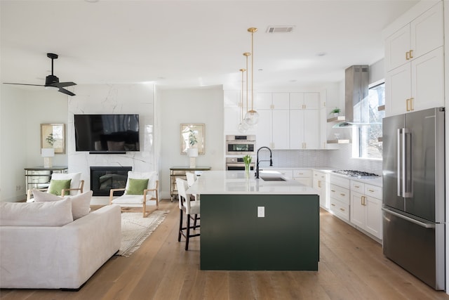 kitchen with sink, appliances with stainless steel finishes, white cabinetry, an island with sink, and decorative light fixtures