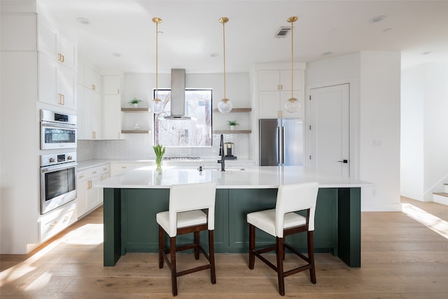 kitchen featuring white cabinetry, stainless steel appliances, a kitchen breakfast bar, island range hood, and an island with sink