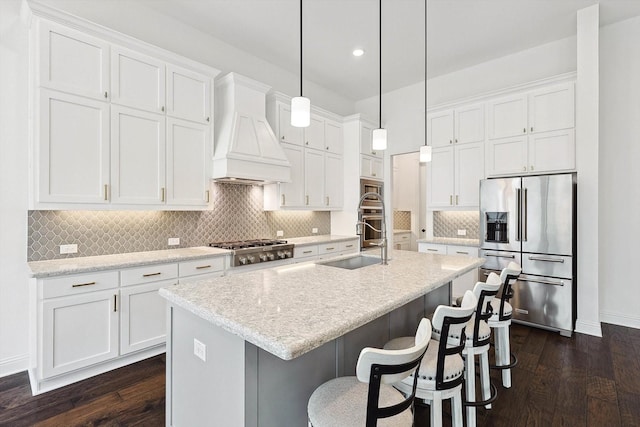 kitchen with appliances with stainless steel finishes, custom range hood, a center island with sink, and white cabinets