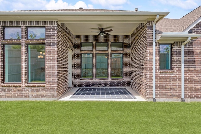 view of exterior entry featuring a lawn and ceiling fan