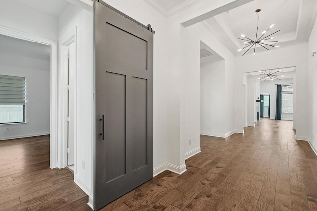 hall with crown molding, dark wood-type flooring, a notable chandelier, a tray ceiling, and a barn door