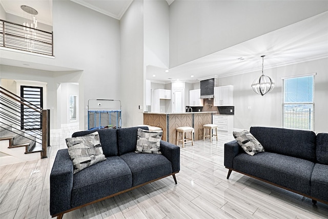 living room with crown molding, a towering ceiling, a notable chandelier, and light hardwood / wood-style floors