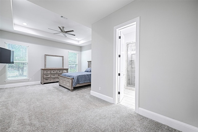 bedroom featuring a raised ceiling, ensuite bathroom, light colored carpet, and multiple windows