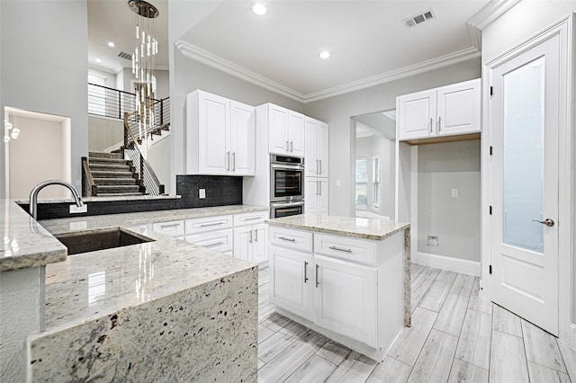 kitchen with sink, white cabinetry, light stone counters, double oven, and pendant lighting