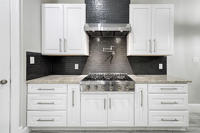 kitchen featuring wall chimney exhaust hood, stainless steel gas stovetop, light stone countertops, decorative backsplash, and white cabinets