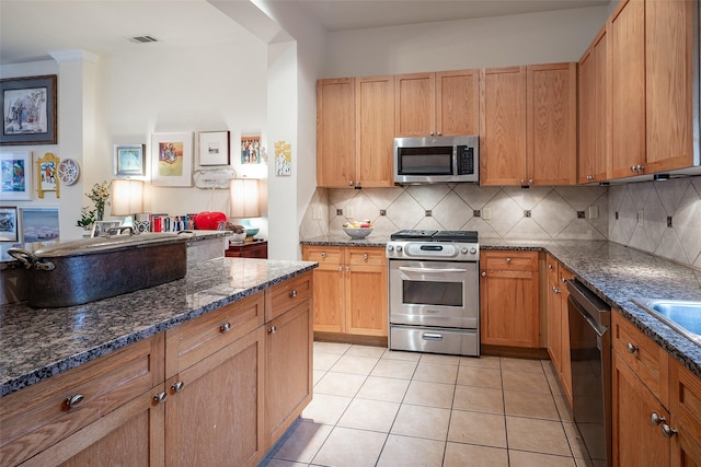 kitchen featuring appliances with stainless steel finishes, light tile patterned floors, decorative backsplash, and dark stone counters