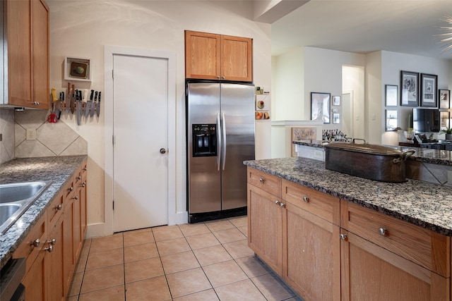 kitchen with light tile patterned floors, stainless steel fridge, dishwasher, dark stone countertops, and decorative backsplash