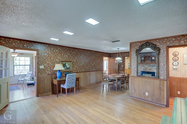 interior space with ornamental molding, hanging light fixtures, a textured ceiling, and light hardwood / wood-style flooring