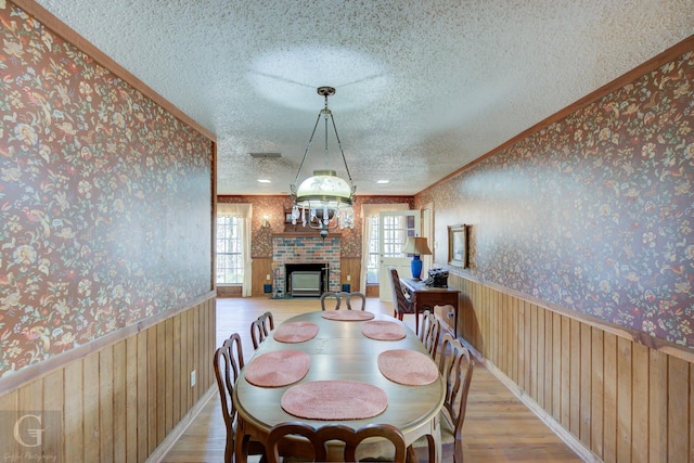 dining space featuring crown molding, wooden walls, light hardwood / wood-style floors, and a textured ceiling