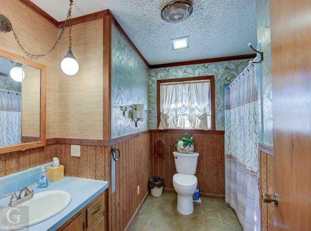 bathroom featuring vanity, ornamental molding, a textured ceiling, toilet, and wood walls