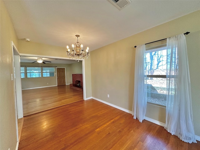 empty room featuring wood-type flooring, ceiling fan with notable chandelier, and a brick fireplace