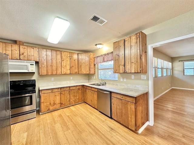 kitchen with stainless steel appliances, plenty of natural light, sink, and light hardwood / wood-style floors