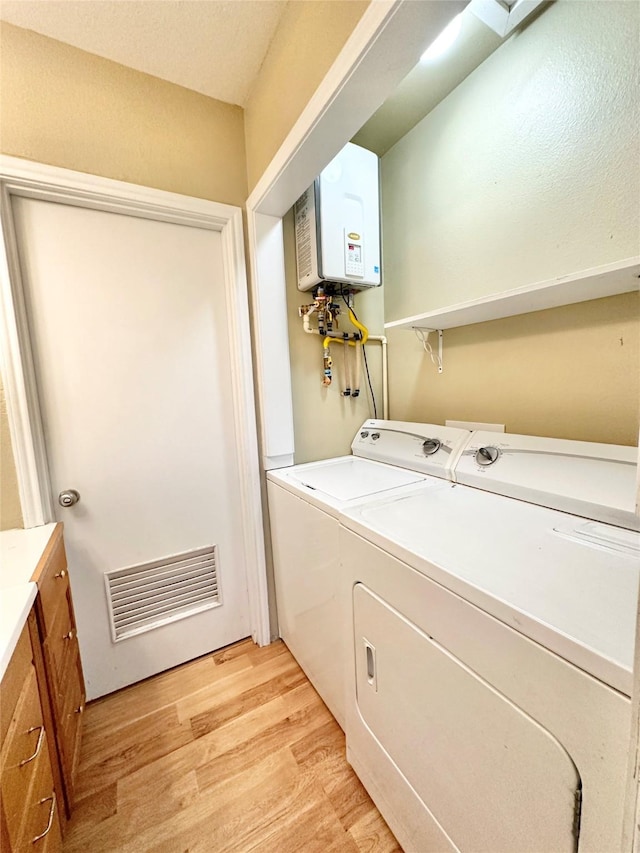 laundry area featuring water heater, washer and dryer, and light wood-type flooring