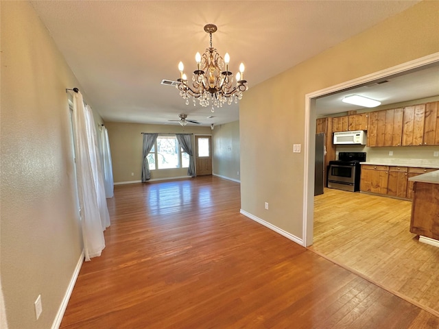 unfurnished dining area featuring ceiling fan with notable chandelier and light hardwood / wood-style floors