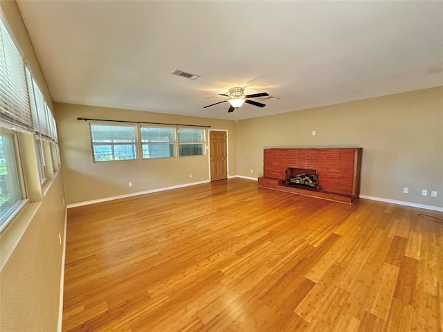 unfurnished living room with ceiling fan, a brick fireplace, and light wood-type flooring