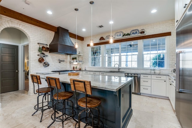 kitchen featuring a kitchen island, appliances with stainless steel finishes, white cabinets, custom exhaust hood, and light stone counters