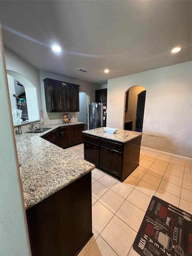 kitchen featuring a sink, freestanding refrigerator, a center island, visible vents, and arched walkways