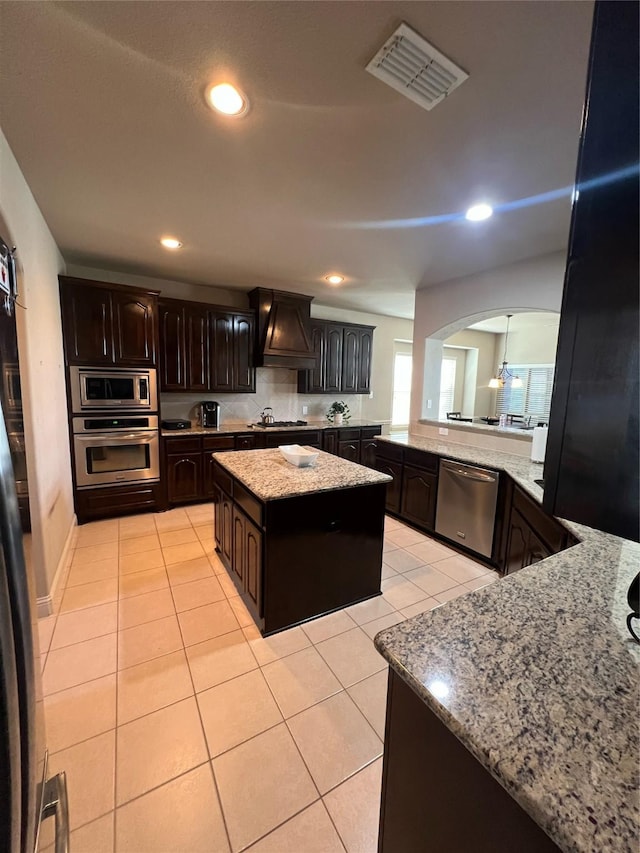 kitchen with visible vents, custom exhaust hood, appliances with stainless steel finishes, arched walkways, and light tile patterned floors