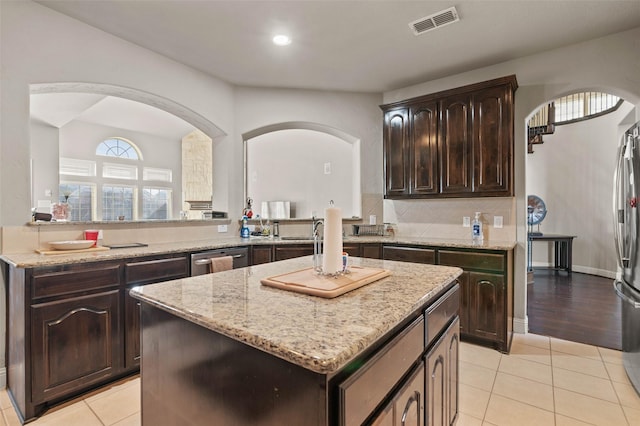kitchen featuring dark brown cabinetry, a center island, light tile patterned floors, visible vents, and arched walkways