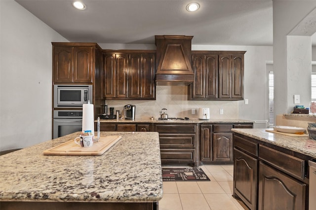 kitchen featuring decorative backsplash, dark brown cabinets, custom range hood, and appliances with stainless steel finishes