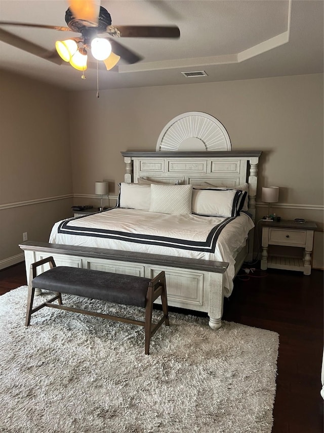 bedroom with a tray ceiling, wood finished floors, baseboards, visible vents, and ceiling fan