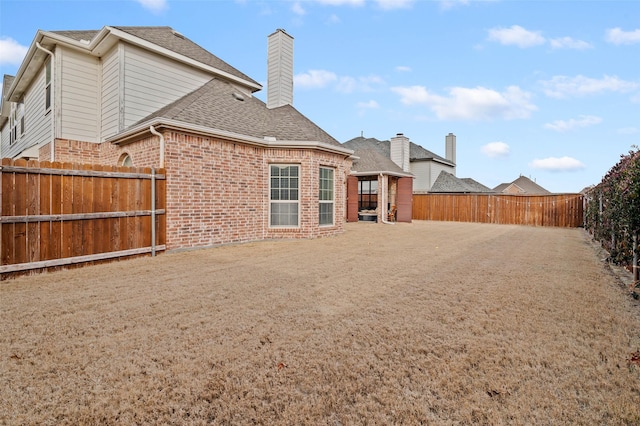 back of house featuring a fenced backyard, brick siding, a shingled roof, and a chimney