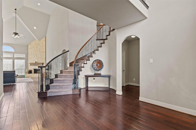 stairs with high vaulted ceiling, hardwood / wood-style floors, a fireplace, and ceiling fan