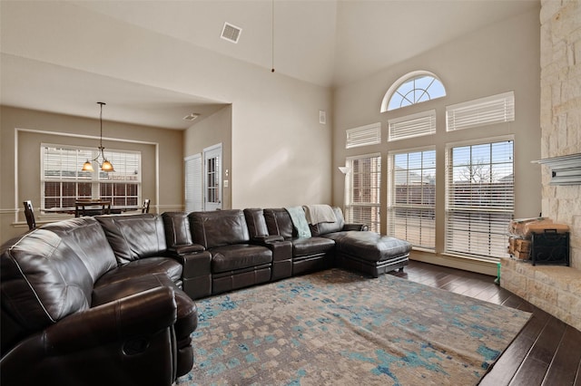 living room with a notable chandelier, a fireplace, wood finished floors, visible vents, and a towering ceiling