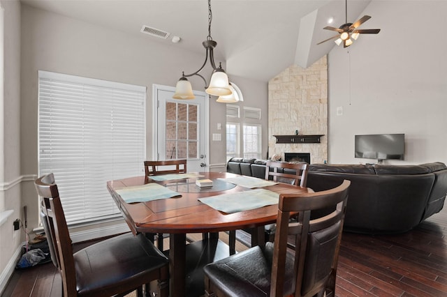 dining room with ceiling fan, dark hardwood / wood-style flooring, high vaulted ceiling, and a stone fireplace