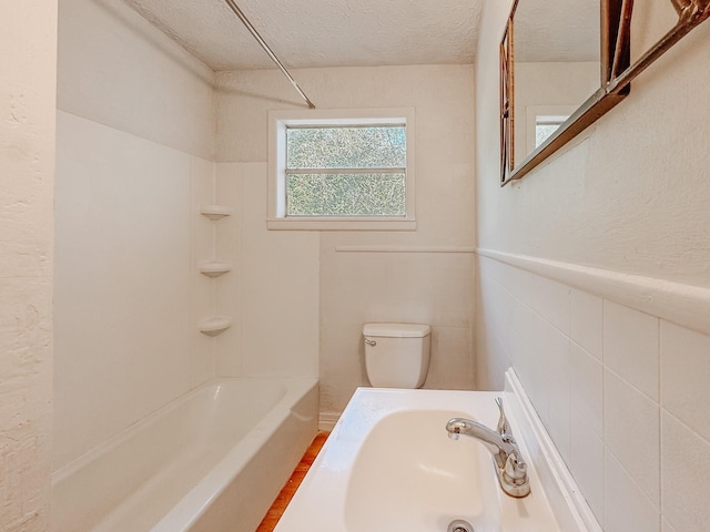 bathroom with a textured ceiling, tile walls, shower / washtub combination, a sink, and toilet