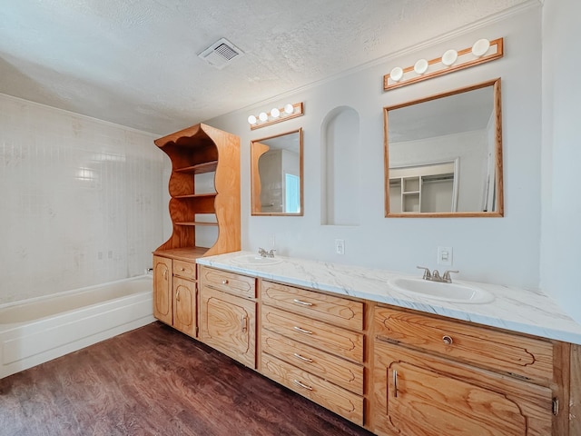 full bath with a textured ceiling, visible vents, a sink, and wood finished floors