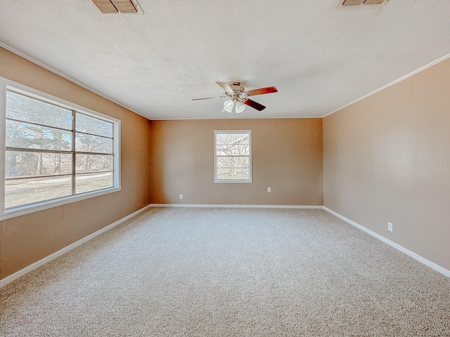 carpeted empty room featuring crown molding, a textured ceiling, a ceiling fan, baseboards, and visible vents