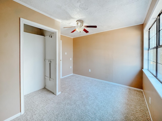 unfurnished bedroom featuring ceiling fan, a textured ceiling, baseboards, ornamental molding, and carpet