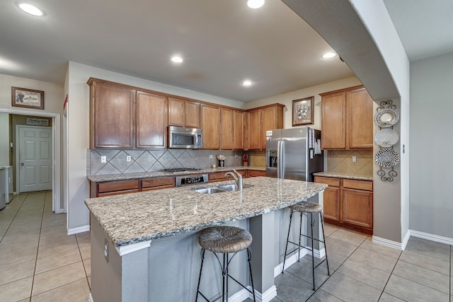 kitchen with light tile patterned flooring, stainless steel appliances, a breakfast bar, a sink, and a center island with sink